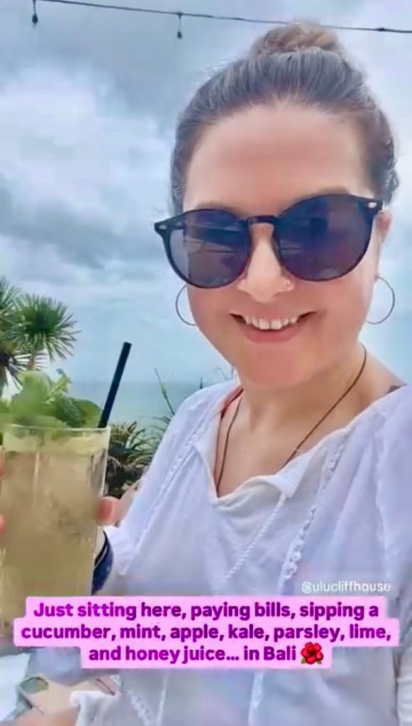 Woman entrepreneur in sunglasses holding a cold drink with tropical palms behind her on a bleisure business trip
