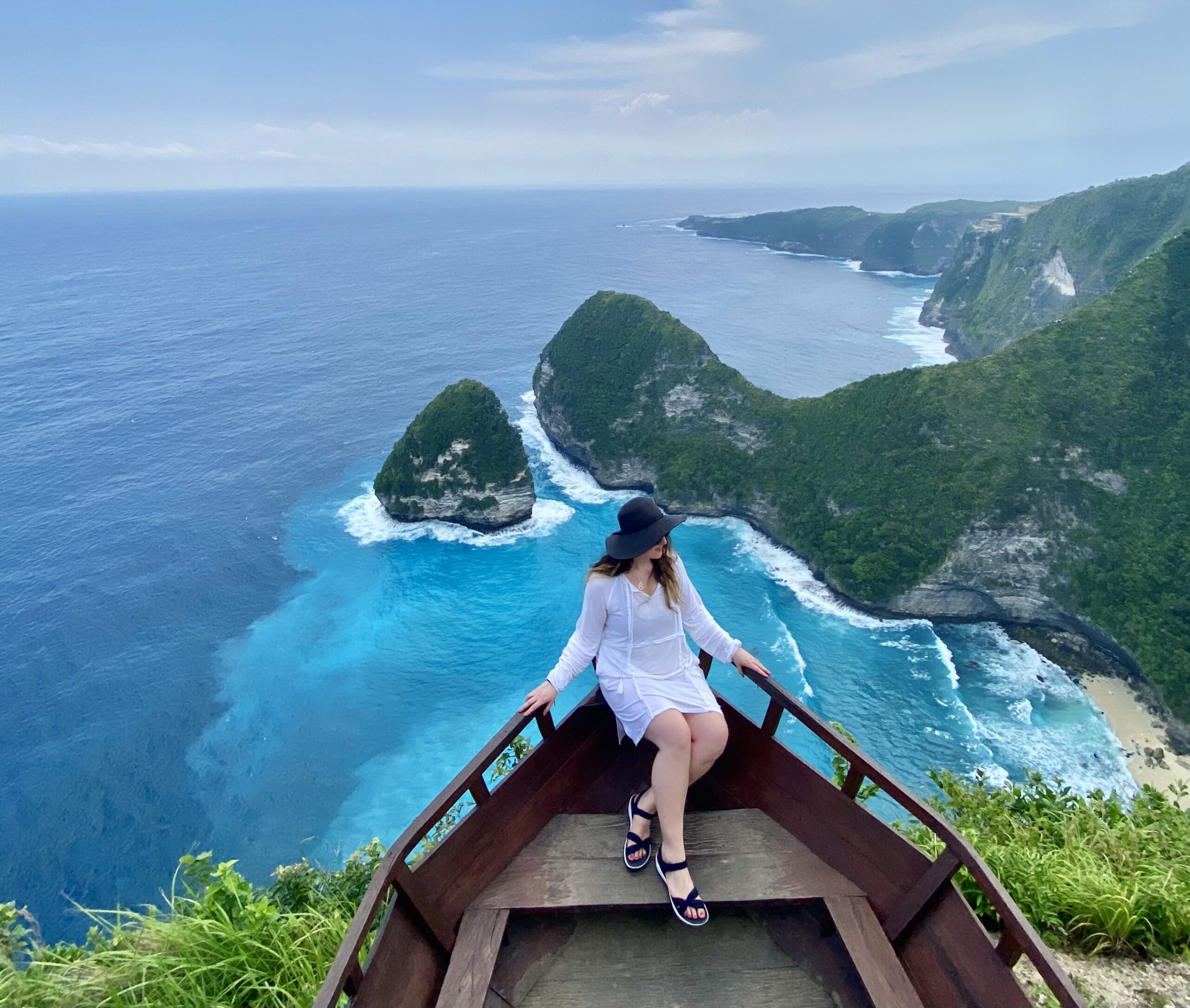 Woman entrepreneur sitting on the bow of a wooden boat looking out over the turquoise bay at Nusa Penida in Bali